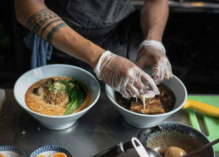 A chef making ramen while wearing gloves.